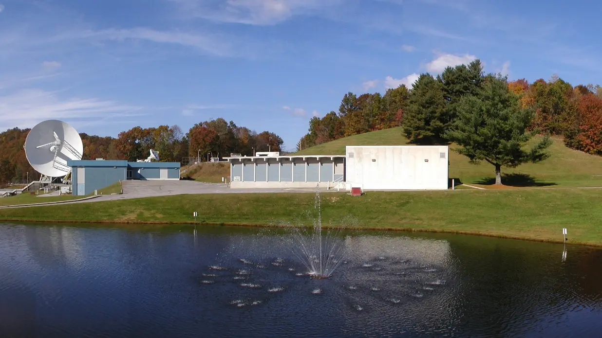 دریاچهای با فواره در مقابل چندین ساختمان بتنی و یک دیش تلسکوپ رادیویی بزرگ