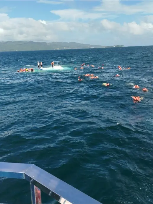 افراد با جلیقه‌های نجات در دریا اطراف یک کتاماران نیمه‌غوطه‌ور.