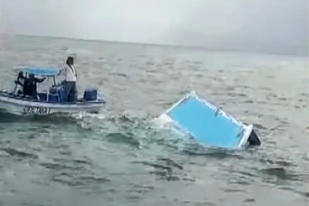 قایقی با دو نفر که در حال رسیدگی به یک کتاماران واژگون در آب هستند.