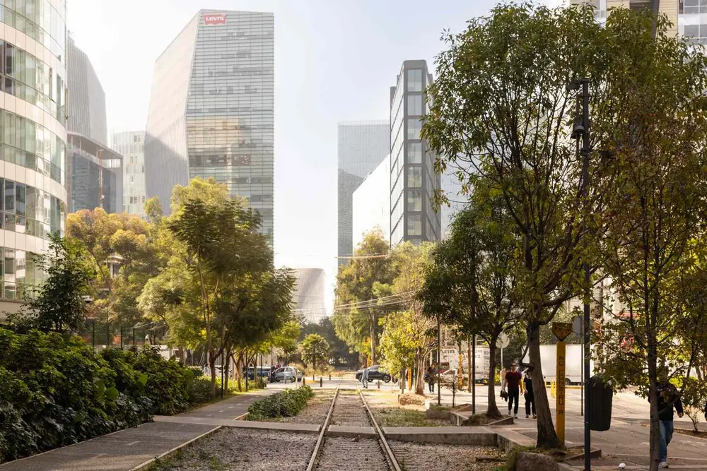 خیابان شهری در مکزیکو سیتی با درختان، ریلهای راهآهن و ساختمانهای مدرن