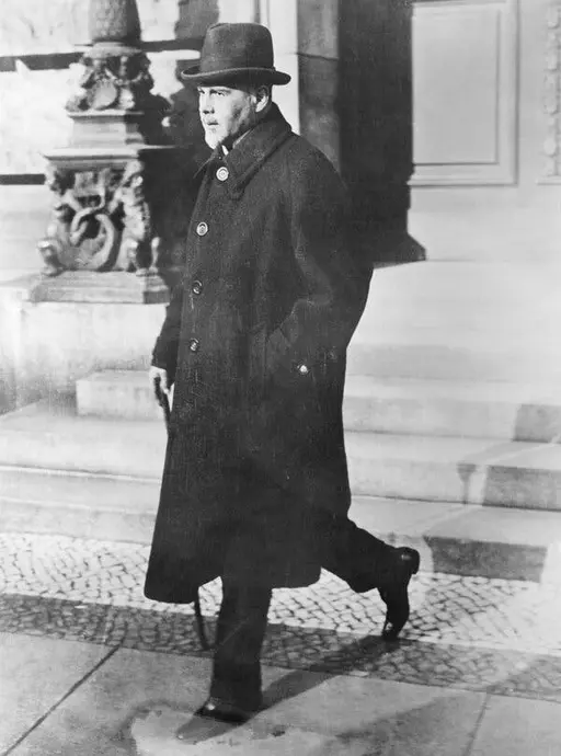 عکسی سیاهسفید مردی در شانهقوی، پوشیده در کت بلند و کلاه، والتر راثنائو را در سال ۱۹۲۲، در حال پایین رفتن از پلهها به تصویر میکشد.