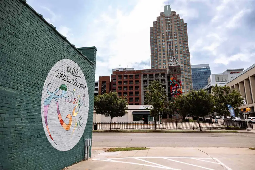 دیوار آجری با نقاشی دیواری «به رالی، همه خوش‌آمدید» در کنار آسمان‌خراش در محیط شهری