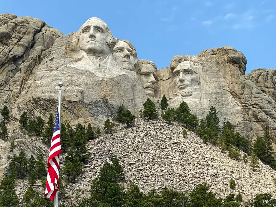 تصویری از مانت رشت‌مور با پرچم آمریکا در پیش‌زمینه.