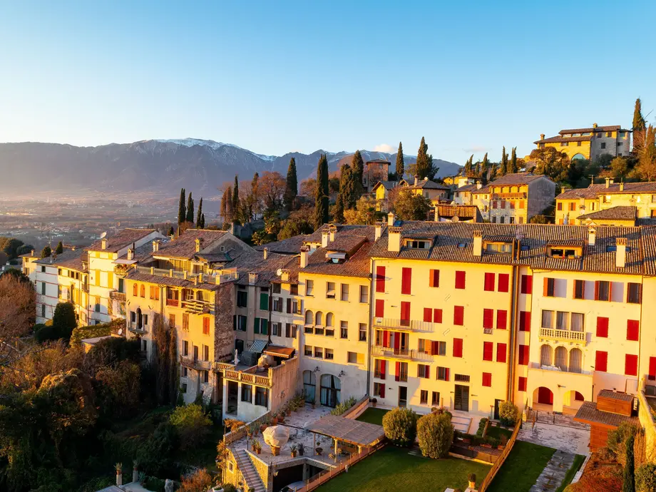 خانهها بر روی تپهای چیدهاند و در دوردست کوهها و درختان دیده میشوند.