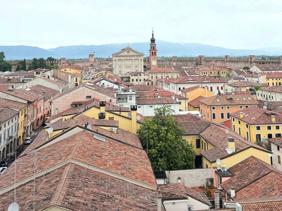 نمای هوایی یک شهر ایتالیایی شامل خانهها، کلیسا و کوهها.