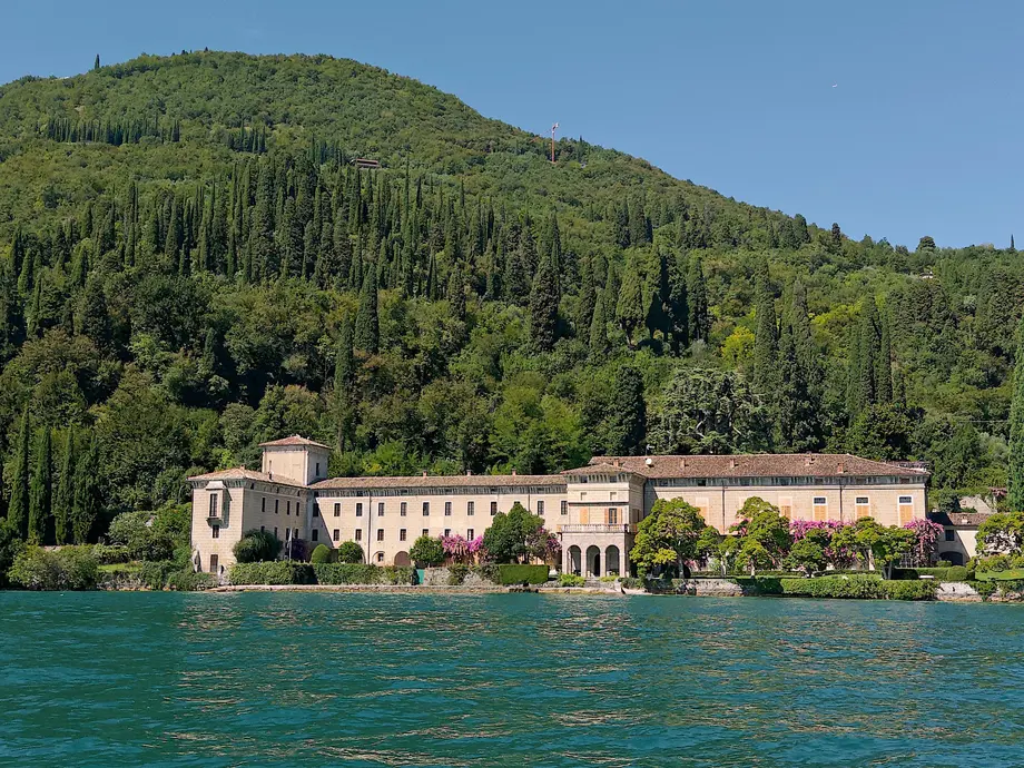 ساختمان بزرگی که توسط درختان احاطه شده است؛ جلوی دریاچه و پسزمینه کوههای پوشیده از درختان.