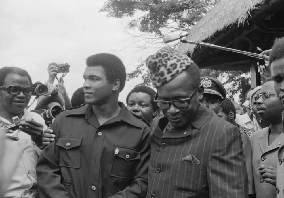 رئیسجمهور زائیر موبوتو همراه با مبارز سنگینوزن محمد علی در حال قدم زدن در باغهای کاخ ریاست جمهوری در تاریخ ۲۸ اکتبر ۱۹۷۴