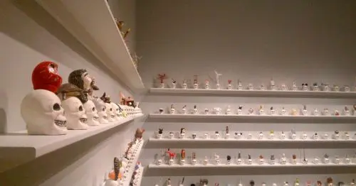 مجموعه‌ای از آثار هنری شبیه به جمجمه‌ها بر روی قفسه‌ای در مقابل دیوار سفید.