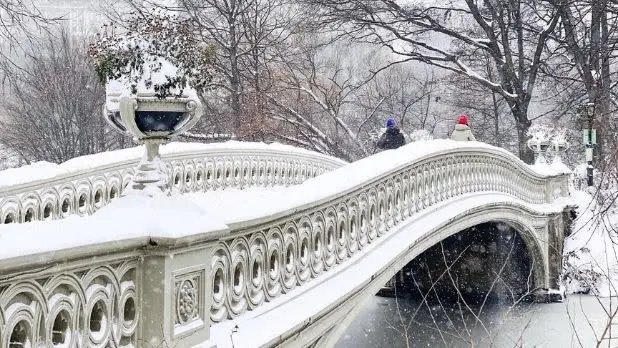 دو نفر که روی پلی پوشیده از برف در پارک سنترال قدم میزنند