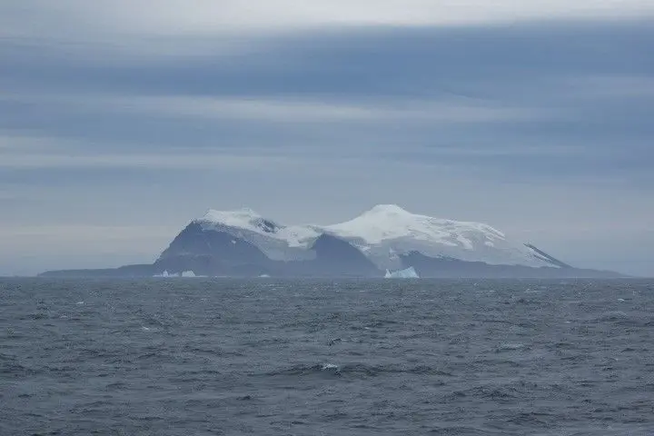 این عکس جزیرهٔ Candlemas را نشان می‌دهد که از دور کمی کدر به‌نظر می‌رسد، با اقیانوسی موج‌دار در پیش‌زمینه و آسمانی نیمه‌ابری در پس‌زمینه. جزیره در پایه‌اش تاریک و سنگی است و با یخ‌های یخی پوشیده شده است.