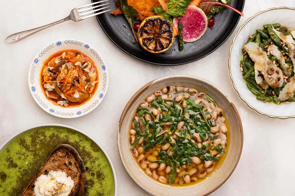 گزینشی از غذاهای سینی‌شده شامل سوپ، سبزیجات کبابی و نان تست با کرم، که بر روی یک میز به همراه کارد و چنگال‌ها قرار گرفته است