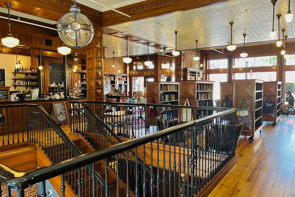 درون یک کتابفروشی یا کتابخانه با یک پلکان مرکزی، قفسه‌های کتاب و چراغ‌های آویزان سقفی