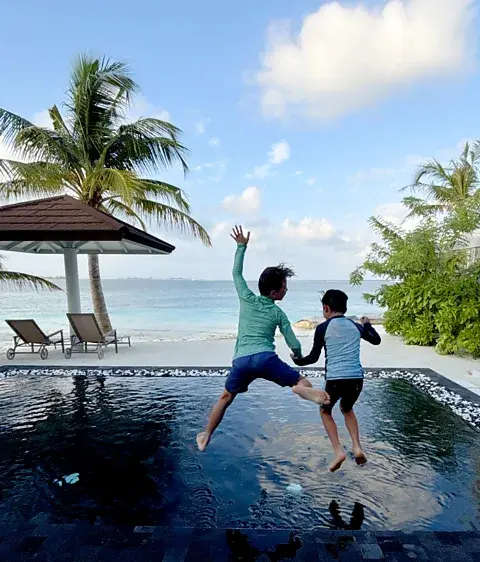 کارمن رابرتس دو پسر در حال پریدن به استخر شنا در مالدیو با اقیانوس در پسزمینه (منبع: کارمن رابرتس)
