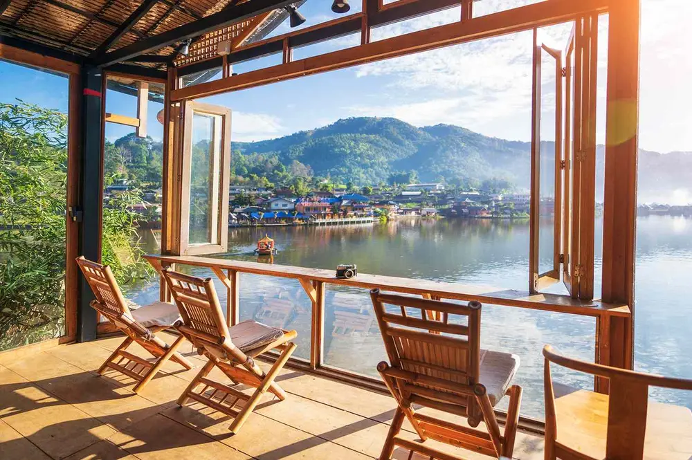 نمایی زیبا از دریاچه و کوهها از عرشهٔ چوبی با صندلیها و پنجرههای باز