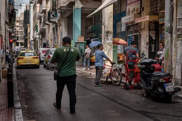 خیابانی باریک و شلوغ با مردم و وسایل نقلیه. مغازهها با چترهای باز در کنار خیابان قرار دارند و روی یکی از تابلوها نوشته شده «EuroBangla Stores».