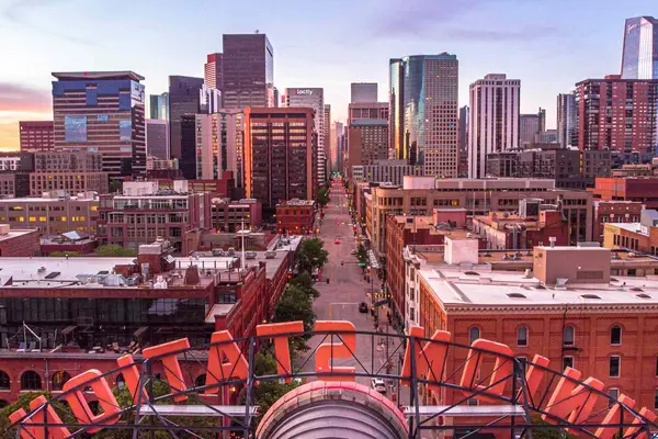 نمای آسمانخراشهای دنور در غروب آفتاب از زاویهای بالا با تمرکز بر ساختمانهای مرکز شهر و سازههای قرمز در پیشزمینه